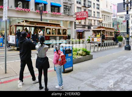 San Francisco Cable Cars auf der Powell & Hyde Line auf der Powell Street vorbei am Hotel Stratford mit einer Familie, die San Francisco Kalifornien USA beobachtet Stockfoto