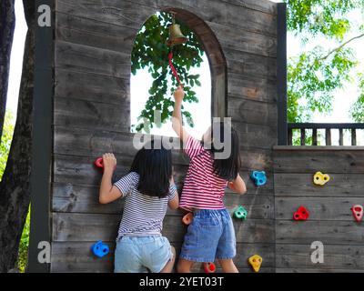 Kinder spielen im Freien auf einem Holzspielplatz in einem Park. Glückliches Mädchen, das im Sommer auf einer hölzernen Kletterwand auf dem Spielplatz spielt. Stockfoto