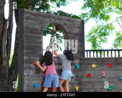 Kinder spielen im Freien auf einem Holzspielplatz in einem Park. Glückliches Mädchen, das im Sommer auf einer hölzernen Kletterwand auf dem Spielplatz spielt. Stockfoto