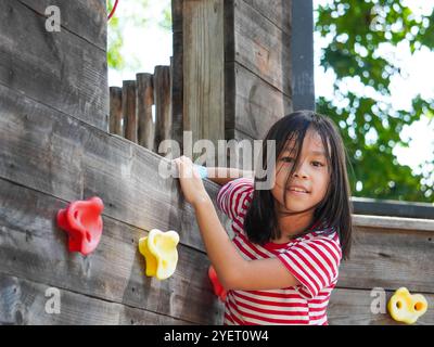 Kinder spielen im Freien auf einem Holzspielplatz in einem Park. Glückliches Mädchen, das im Sommer auf einer hölzernen Kletterwand auf dem Spielplatz spielt. Stockfoto