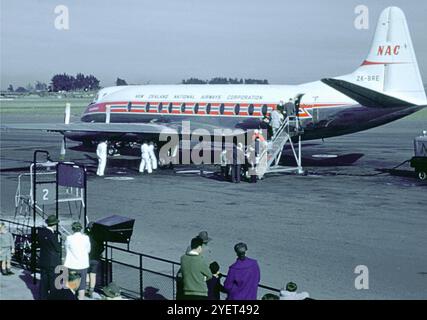 Passagiere, die in den 1960er Jahren ein Flugzeug der New Zealand National Airways Corporation (NAC) der Vickers Viscount 800-Serie mit der Zulassung ZK-BRE auf dem Asphalt besteigen Dieses ikonische Turboprop-Flugzeug war ein wichtiger Bestandteil der NAC-Flotte und bediene regionale und nationale Routen durch Neuseeland. Die Vickers Viscount war eines der ersten erfolgreichen Turboprop-Flugzeuge, bekannt für ihre Geschwindigkeit, ihren Komfort und ihre Zuverlässigkeit, was eine bedeutende Entwicklung in der kommerziellen Luftfahrt Mitte des 20. Jahrhunderts darstellt. Bodenbesatzung und Zuschauer beobachten aus der Nähe. Stockfoto