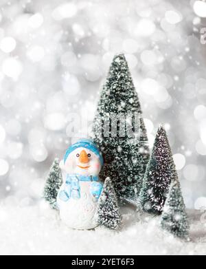 Spielzeug Schneemann auf Schnee zwischen Tannen mit Schneefall. Weihnachtsgrußkarte Vorlage für Weihnachten oder Neujahr Stockfoto
