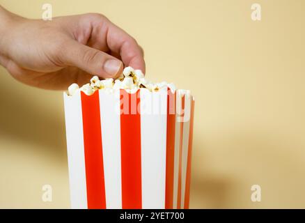 Männliche Hand, die Popcorn aus einem roten Pappeimer mit weißen Streifen aufnimmt, Restaurant- und Unterhaltungskonzept Stockfoto