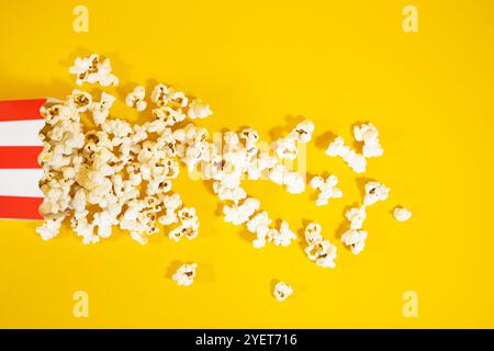 Draufsicht auf roten Kartoneimer mit weiß liegendem Eimer. Verbreitetes Popcorn auf gelbem Hintergrund, Konzept von Essen und Kinounterhaltung Stockfoto