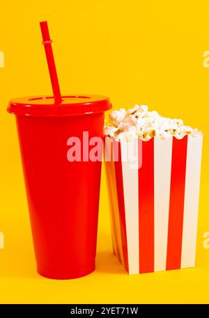 Vertikales Bild des weiß-weiß gestreiften Pappeimer mit Popcorn und roter Soda Tasse auf gelbem Hintergrund, Konzept des Essens im Kino und Unterhaltung Stockfoto