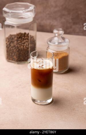 Kaffee mit Kokosmilch und Eiswürfeln in einem hohen Glas. Traditionelles alkoholfreies kaltes Getränk. Im Hintergrund ein Glas Kaffee und ein Glas Zucker. S Stockfoto