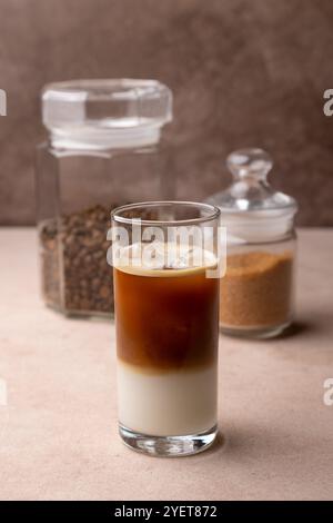 Kaffee mit Kokosmilch und Eiswürfeln in einem hohen Glas. Traditionelles alkoholfreies kaltes Getränk. Im Hintergrund ein Glas Kaffee und ein Glas Zucker. S Stockfoto