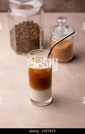 Kaffee mit Kokosmilch und Eiswürfeln in einem hohen Glas. Traditionelles alkoholfreies kaltes Getränk. Im Hintergrund ein Glas Kaffee und ein Glas Zucker. S Stockfoto