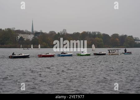 Hamburg, Deutschland. November 2024. Segelboote werden bei bewölktem Herbstwetter von einem Motorboot über die Außenalster gezogen. Quelle: Marcus Brandt/dpa/Alamy Live News Stockfoto