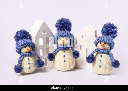 Gestrickter Schneemann in blauem Hut und Schal mit weißen Häusern auf grauem Hintergrund. Wintermärchen mit eigenen Händen, Hobby. Frohe Weihnachten und ne Stockfoto