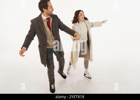 Glückliches Paar kleidete sich warm und stilvoll Winterkleidung, lachte und hielt Hände, während sie zusammen Schlittschuh laufen. Fröhlicher Wintermoment Stockfoto