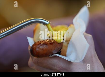 Hamburg, Deutschland. November 2024. Auf dem Wandsbeker Winterzauber Weihnachtsmarkt nimmt eine Besucherin Senf zu ihrer gegrillten Wurst. Quelle: Marcus Brandt/dpa/Alamy Live News Stockfoto