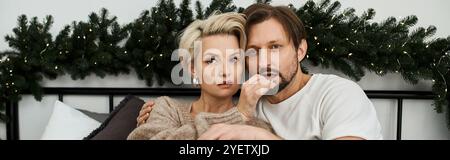 Ein Paar kuschelt sich auf ein gemütliches Bett, umgeben von festlicher Dekoration und Wärme. Stockfoto