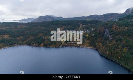 Aus der Vogelperspektive auf einen ruhigen See umgeben von dichtem Wald und Bergen unter einem bewölkten Himmel. Mit Gebäuden auf einem Hügel in der Nähe eines Sees Stockfoto
