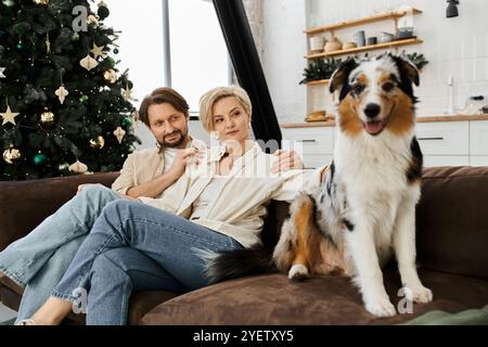 Ein Paar entspannt sich auf einem Sofa, teilt Wärme und Lächeln, während ihr Hund glücklich in der Nähe sitzt. Stockfoto