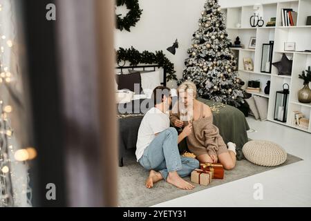 Ein glückliches Paar genießt während der Weihnachtszeit einen herzlichen Moment zusammen auf einem weichen Teppich. Stockfoto
