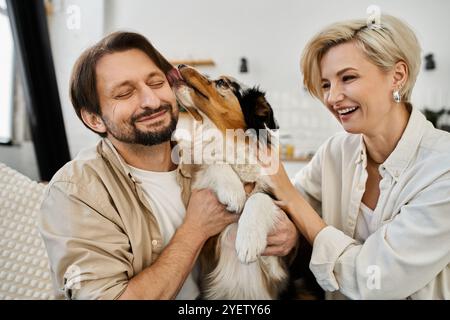 Ein glückliches Paar teilt Lachen und Zuneigung, während ihr Hund den Mann spielerisch leckt. Stockfoto