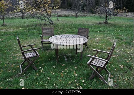 Dieses Bild zeigt eine rustikale Sitzanordnung im Freien mit einem runden Holztisch und vier Holzstühlen auf grünem Gras. Die Szene ist umgeben von Stockfoto