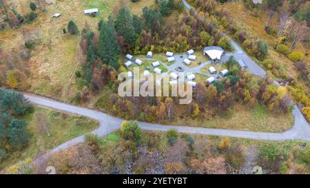 Blick aus der Vogelperspektive auf einen Campingplatz mit mehreren Zelten, die in einem kreisförmigen Muster angeordnet sind, umgeben von Bäumen und Grün. Stockfoto