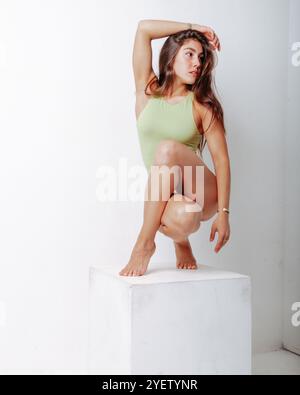 Selbstbewusst und elegant posiert eine Frau in einem minimalistischen Studio und zeigt Schönheit und Kraft in einem eleganten grünen Badeanzug vor einem sauberen weißen Hintergrund Stockfoto