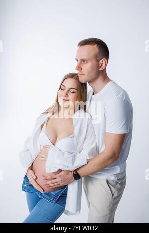 Ein Mann umarmt eine schwangere Frau und streichelt ihren Bauch, ein glückliches junges Paar ist schwanger. Stockfoto