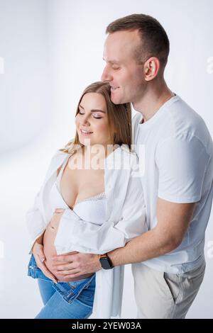 Ein Mann umarmt eine schwangere Frau und streichelt ihren Bauch, ein glückliches junges Paar ist schwanger. Stockfoto