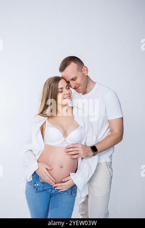 Ein Mann umarmt eine schwangere Frau und streichelt ihren Bauch, ein glückliches junges Paar ist schwanger. Stockfoto