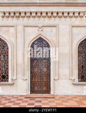 Eine wunderschön gefertigte Holztür verfügt über ein raffiniertes Gitterdesign, das sich an einer traditionellen Steinmauer befindet. Die architektonischen Details unterstreichen die Handwerkskunst in dieser urbanen Lage. Stockfoto