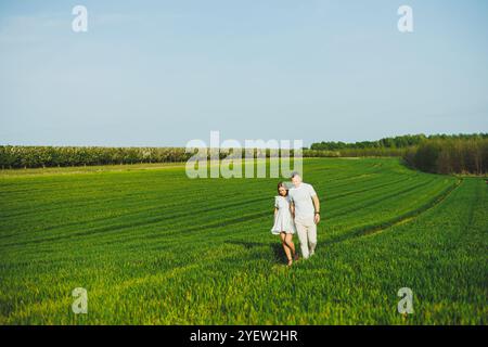 Schwangere Paare umarmt sich in einem grünen Frühlingsfeld. Werdende Eltern im Park der weiß blühenden Bäume. Ein romantisches Paar erwartet ein Baby. Ein Spaziergang Stockfoto