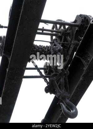 Alte Krandetails isoliert auf weißem Hintergrund. Massive schwarze Zahnräder und andere Teile von Vintage-Industriemaschinen, Schwarzweißfoto, abstraktes Hea Stockfoto