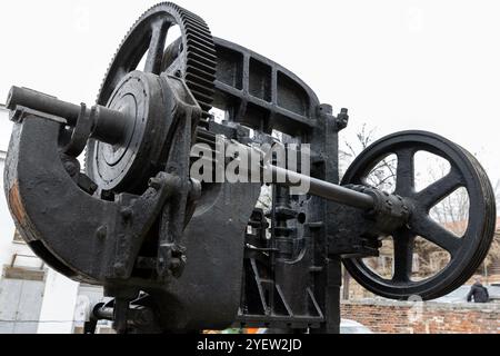 Die Doppelkurbel steht unter hellem Himmel. Massive schwarze Getriebe und andere Teile von Vintage-Industriemaschinen, Nahaufnahme mit selektivem Fokus Stockfoto