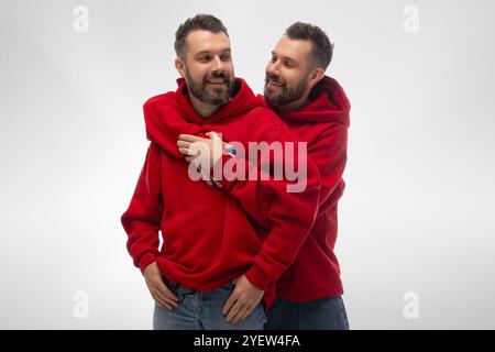 Zwei junge, stilvoll gekleidete Männer, Zwillinge, die zusammen stehen und sich umarmen, drücken Liebe und Unterstützung vor weißem Studiohintergrund aus. Stockfoto