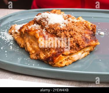 Venedig, Vento – IT – 13. Oktober 2024 Ein Quadrat aus warmer Lasagne auf einer blau-grauen Tafel, bestreut mit geriebenem Käse. Stockfoto