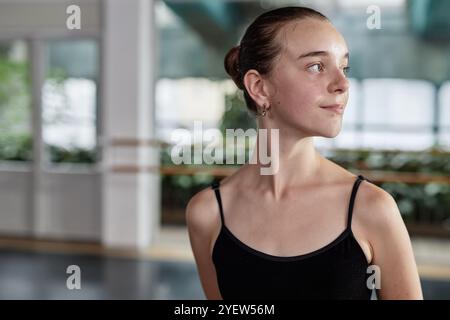 Porträt einer jungen Balletttänzerin mit einem Lächeln auf dem Gesicht, die ein elegantes Trikot zum Üben trägt, während sie vor verschwommenem Hintergrund im Studio und im Kopierraum von der Kamera wegblickt Stockfoto