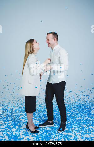 Ein junges glückliches Ehepaar, das sich in blauem Konfetti umarmt. Ein verliebtes Paar freut sich und hat Spaß. Gender-Fotosession Stockfoto