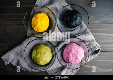 Bunte Kugeln mit geknetem Brotteig in Glasschalen: Gelber, schwarzer, grüner und lila Brotteig mit natürlichen Lebensmittelfarben Stockfoto