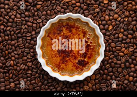 Coffee Creme Brulee umgeben von gerösteten Kaffeebohnen: Flaches Ramekin aus verbranntem Kaffee Creme Brulee umgeben von ganzen Kaffeebohnen Stockfoto