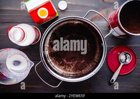 Kaffee-Creme Brulee in einer kleinen Pfanne: Kaffeesatz schwimmt auf Milch und Sahne, umgeben von ihren Behältern und Küchengeräten Stockfoto