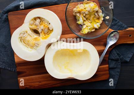Halbierter und gesäumter White Pie Kürbis auf einem Schneidebrett: Samen und Fruchtfleisch aus der Hälfte eines Schneeballkürbis vor dem Rösten im Ofen Stockfoto