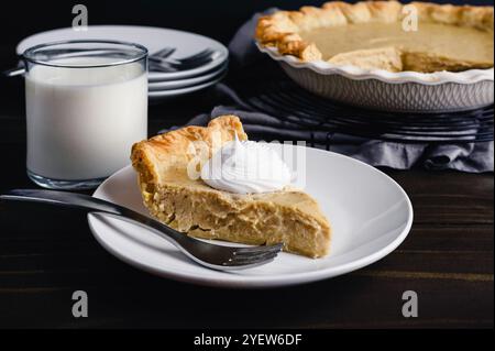 Seitenansicht des weißen Kürbiskuchen mit Schlagsahne: In Scheiben geschnittener Kuchen auf einem kleinen Teller mit einem Glas Milch und zusätzlichen Gabeln und Tellern an der Seite Stockfoto