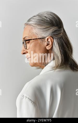 Eine schöne Frau mit grauem Haar strahlt Eleganz in einem weißen Anzug aus, der ihren zeitlosen Stil und ihre Ausgeglichenheit zum Ausdruck bringt. Stockfoto