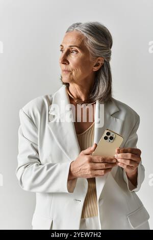 Eine modische, reife Frau strahlt Selbstvertrauen aus, während sie ihr Handy in einem schicken weißen Anzug hält. Stockfoto