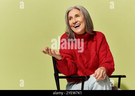 Eine fröhliche Frau mit grauen Haaren lächelt strahlend, während sie im Winter einen kuscheligen roten Pullover trägt. Stockfoto