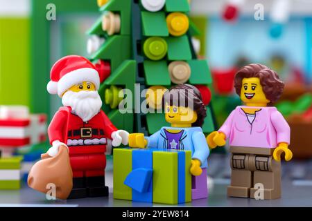 Tambow, Russische Föderation - 17. Oktober 2024 Lego Santa Claus mit Tasche, Mädchen mit Geschenk und ihre Mutter steht neben dem Weihnachtsbaum Stockfoto