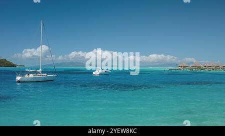 Zwei Segelboote Yachten vor Anker im ruhigen türkisfarbenen Wasser der tropischen Lagune mit Bungalows über dem Wasser. Französisch-Polynesien Bora Bora atemberaubendes tropisches Paradies, perfekter exotischer Sommerurlaub Luxus. Stockfoto