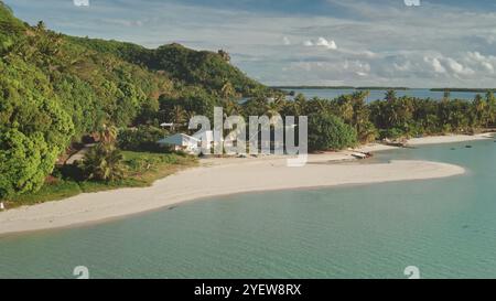 Luftflug über Bungalowhäuser am privaten kleinen Strand. Kristallklares Wasser, weißer Sand, Palmen, grüne Hügellandschaft. Abgelegene wilde Natur tropisches Inselparadies, exotische Urlaubsreise im Sommer Stockfoto