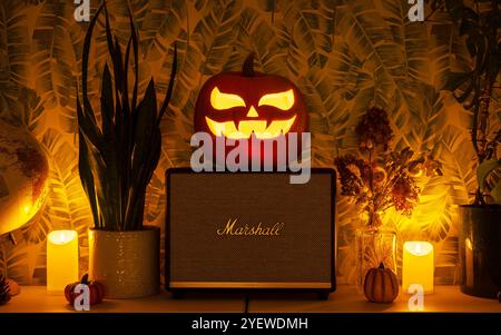 Marshall bluetooth-Lautsprecher im Halloween-Design. Jack-o'-Laterne geschnitzter Kürbis auf den Lautsprecher gestellt, umgeben von Kerzen. Stockfoto