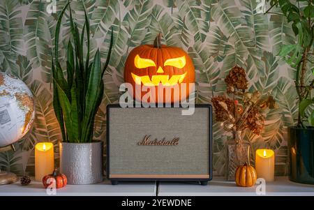 Marshall bluetooth-Lautsprecher im Halloween-Design. Jack-o'-Laterne geschnitzter Kürbis auf den Lautsprecher gestellt, umgeben von Kerzen. Stockfoto