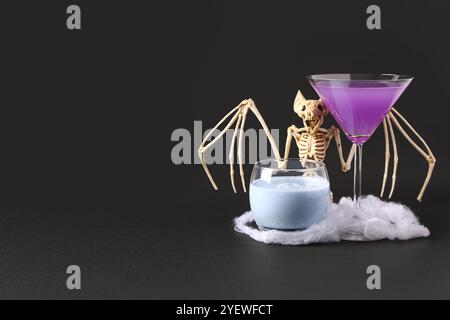 Gläser köstlicher Cocktails mit gruseligen Skelett auf schwarzem Hintergrund. Halloween-Konzept Stockfoto