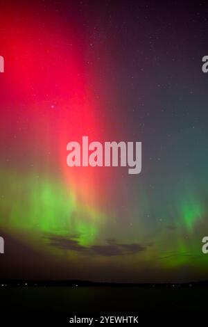 Leuchtende rote und grüne Auroras (Nordlichter) bemalen den Nachthimmel und schaffen eine faszinierende und surreale Atmosphäre über der Grand Traverse Bay, Michigan, Stockfoto